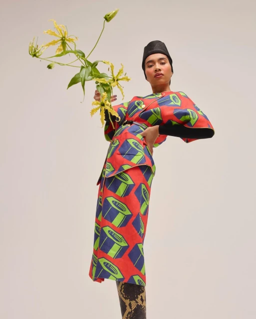 Adult female in a printed red kimono-style outfit poses with yellow tropical flowers against a neutral background in a studio shot.