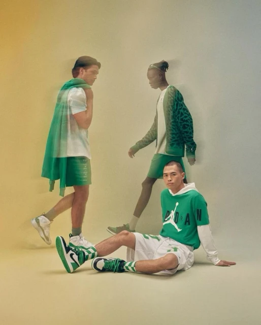 Three male fashion models showcasing green and white Jordan apparel in a studio setting with soft lighting and a gradient backdrop.