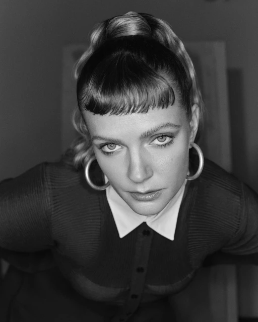 Black and white portrait of a young adult woman with a high ponytail, large hoop earrings, and wearing a button-down shirt with a white collar.