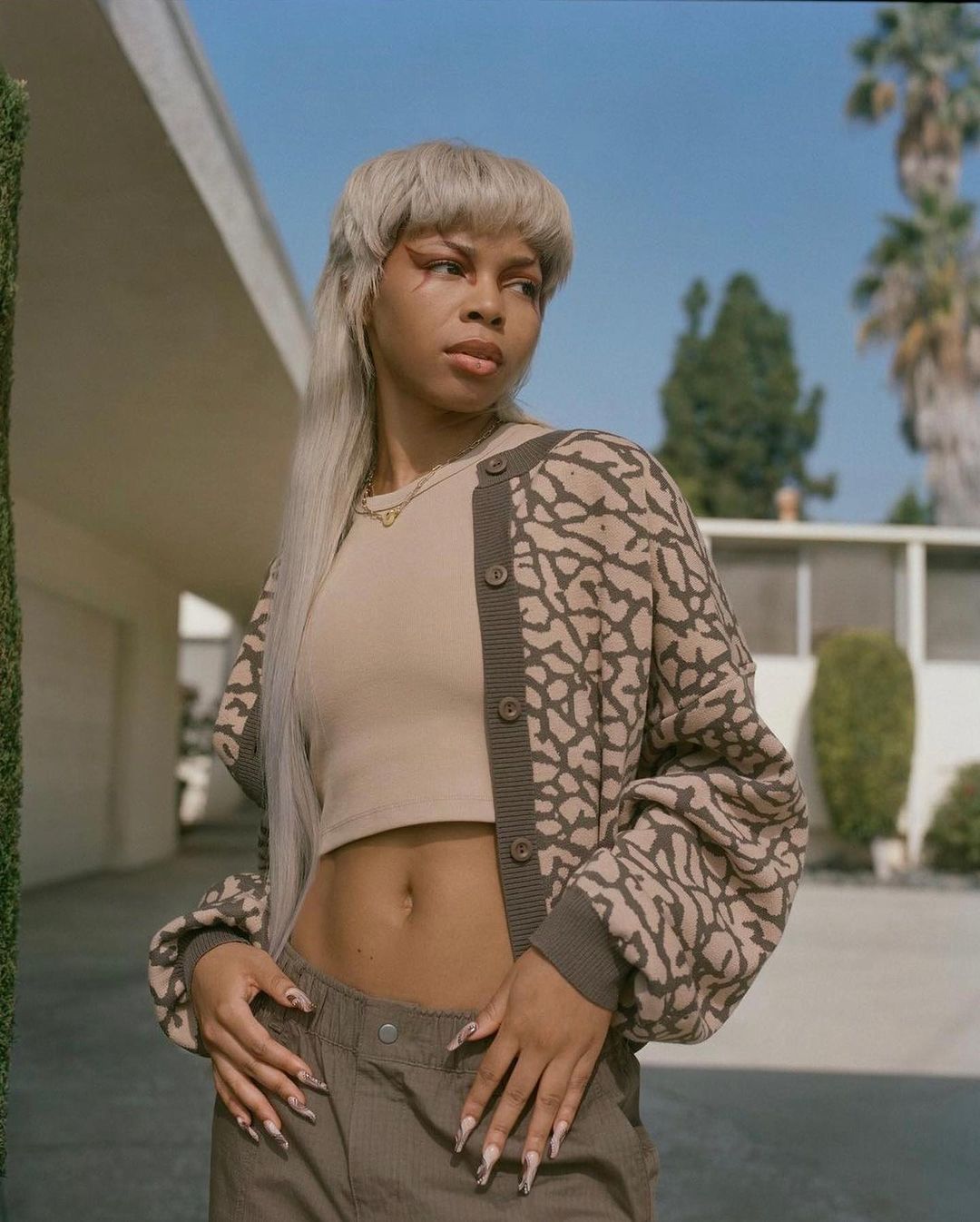 Model with long platinum blonde hair wearing a patterned cardigan and crop top outdoors in New York by Emman Montalvan