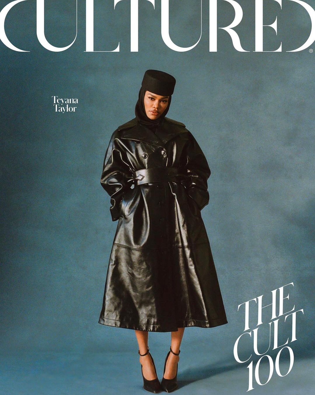Teyana Taylor poses in a full-length shot for Cultured Magazine, wearing a black leather trench coat and matching accessories on a teal backdrop.