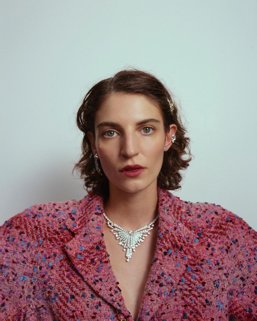 Elegant woman wearing a pink tweed blazer and diamond necklace in a close-up portrait against a white background. Haute couture fashion.