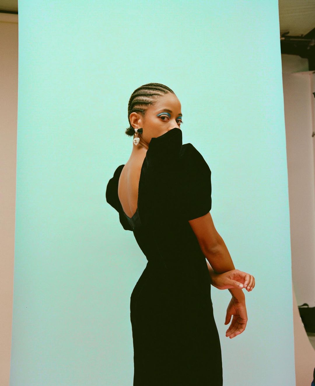 Elegant portrait of a young Black woman in a velvet dress posing against a light blue backdrop, showcasing high fashion and beauty.