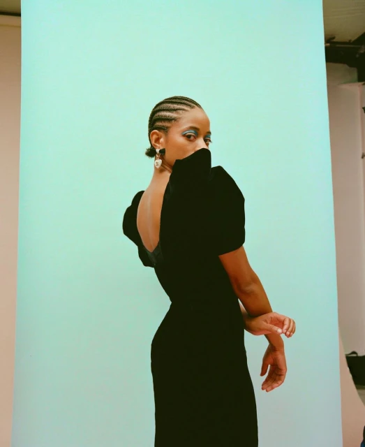Elegant portrait of a young Black woman in a velvet dress posing against a light blue backdrop, showcasing high fashion and beauty.