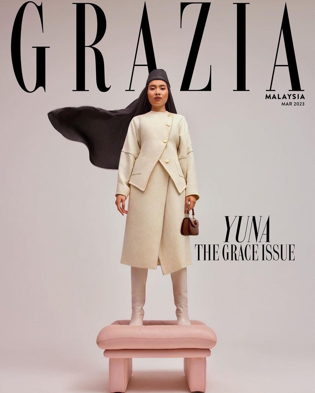 Magazine cover featuring a woman in an off-white outfit and head covering, standing on a pink ottoman against a light backdrop.