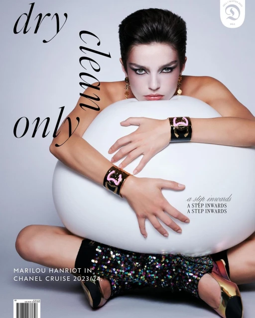Fashion magazine cover featuring a model with dark hair, wearing jewelry and a sparkling dress, seated on a white round prop.