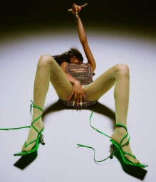 Model in green fishnet tights and strappy green heels posing on a gradient background