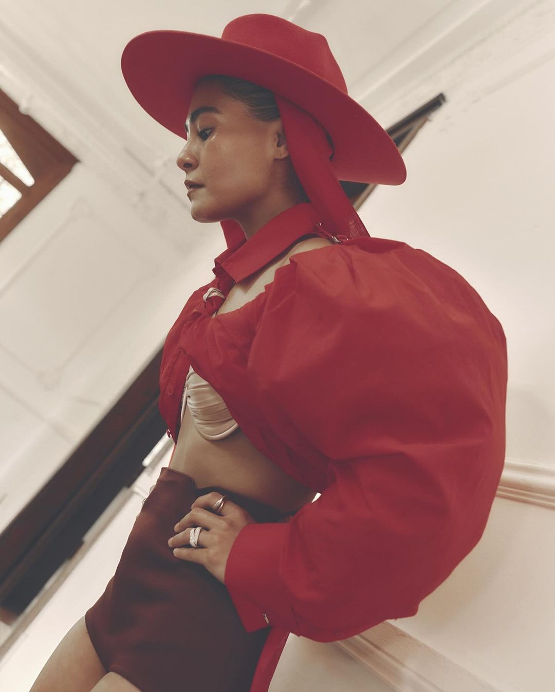 Woman in red hat and blouse poses indoors with hand on hip, showcasing a blend of fashion and confident body language.