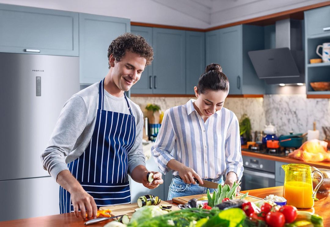 Couple in a kitchen, preparing food together at a wooden counter with fresh vegetables and a modern kitchen in the background.
