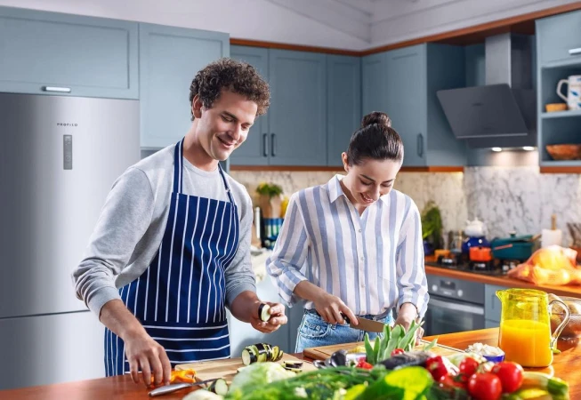 Couple in a kitchen, preparing food together at a wooden counter with fresh vegetables and a modern kitchen in the background.