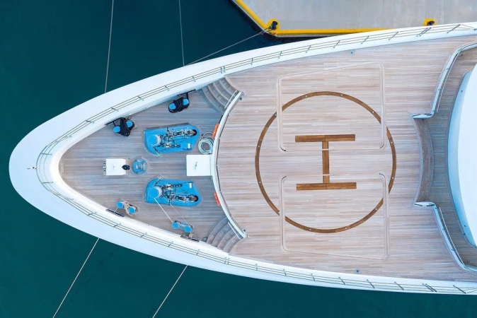 Aerial view of a luxury yacht deck featuring a helipad, seating areas, and equipment, docked in turquoise water on a sunny day.
