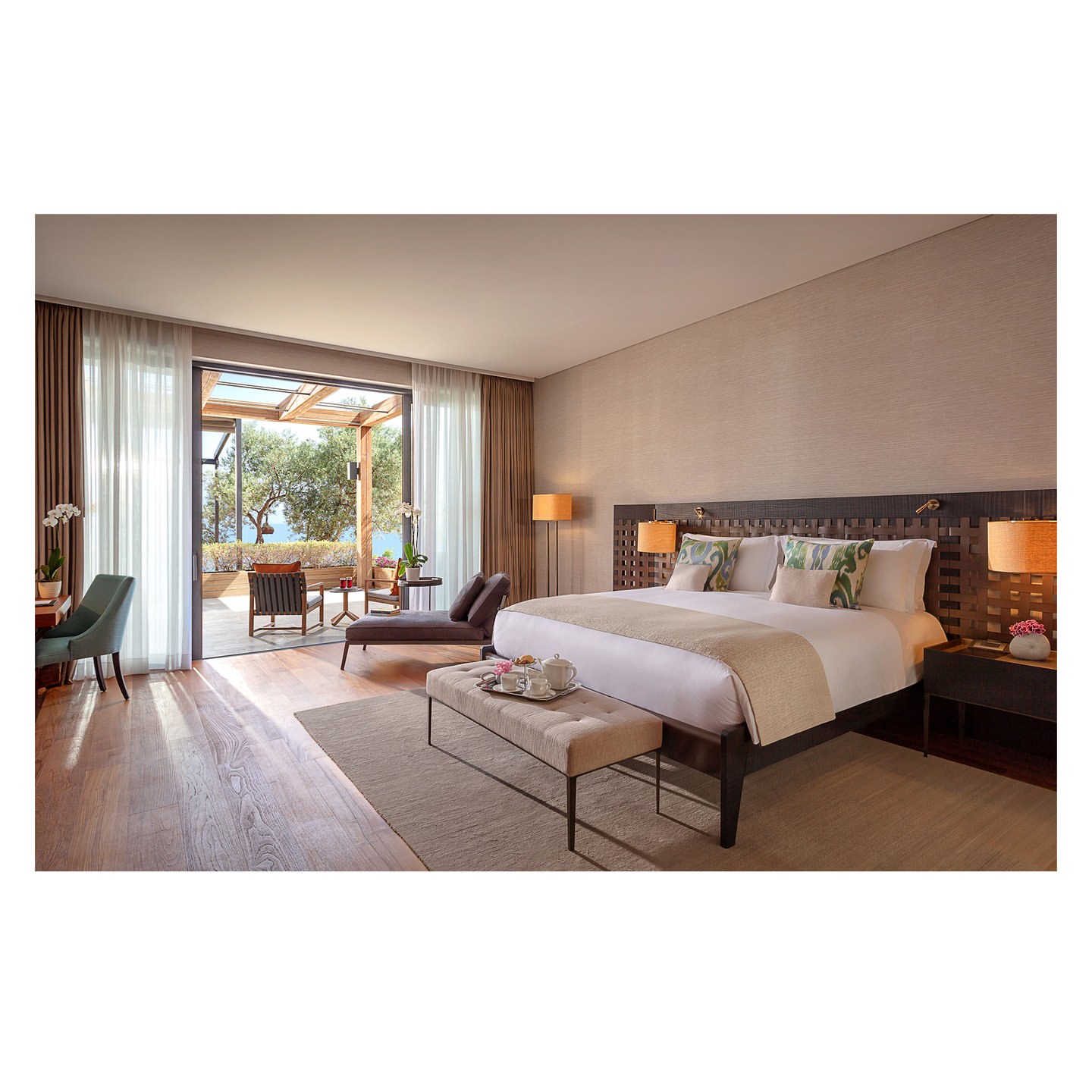 Bedroom interior with a large bed, neutral color scheme, and an outdoor terrace with seating, offering a bright and airy atmosphere.