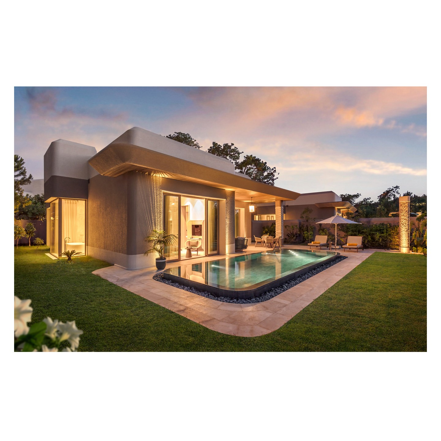 Exterior view of modern home with swimming pool, outdoor furniture, and well-maintained lawn at dusk, showcasing architecture and landscape design.