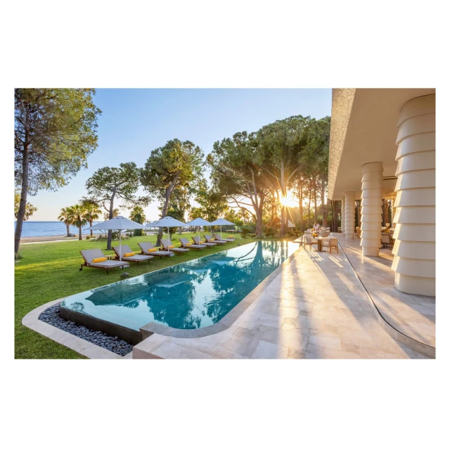 Outdoor resort with a swimming pool, lounge chairs, trees, and building, offering a luxury travel destination on a sunny day.