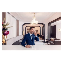 Man in a blue suit talking on his phone while holding an espresso cup in a luxurious hotel lobby in Istanbul.