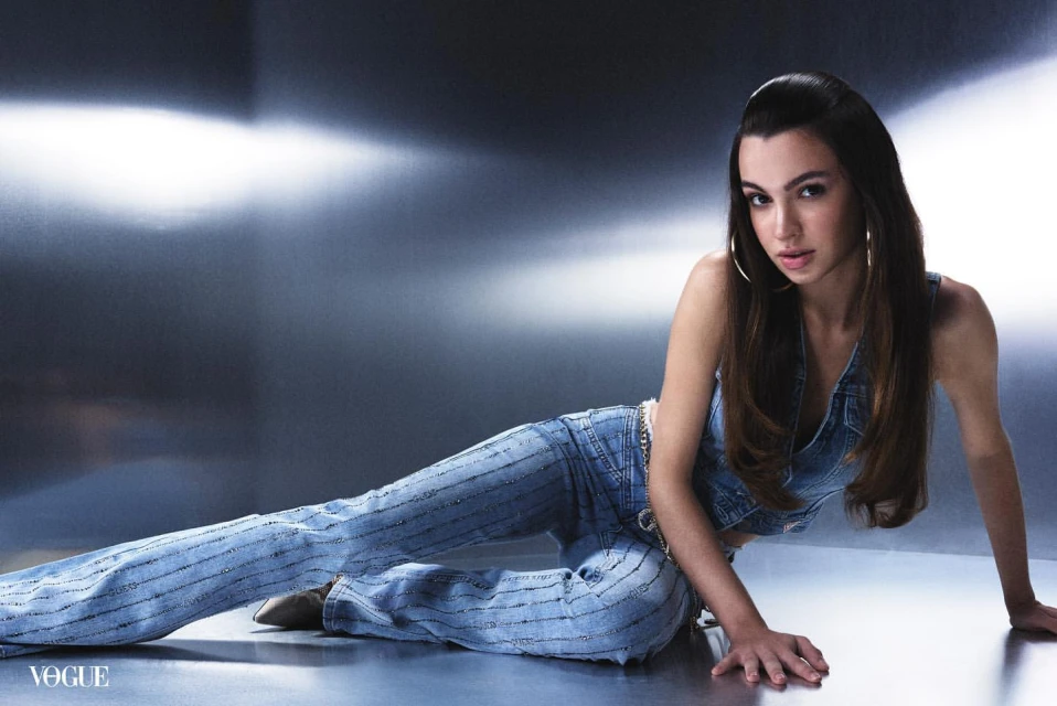 Portrait of a woman in denim clothing, reclining on a reflective surface, medium shot in a studio with cool lighting.