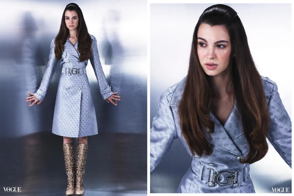 Fashion shot of a woman in a patterned double-breasted trench coat with a wide belt and snake-print boots, posing in a photo studio.