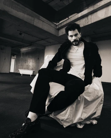 Man seated on a draped chair in an industrial space photographed by Erdi Dogan
