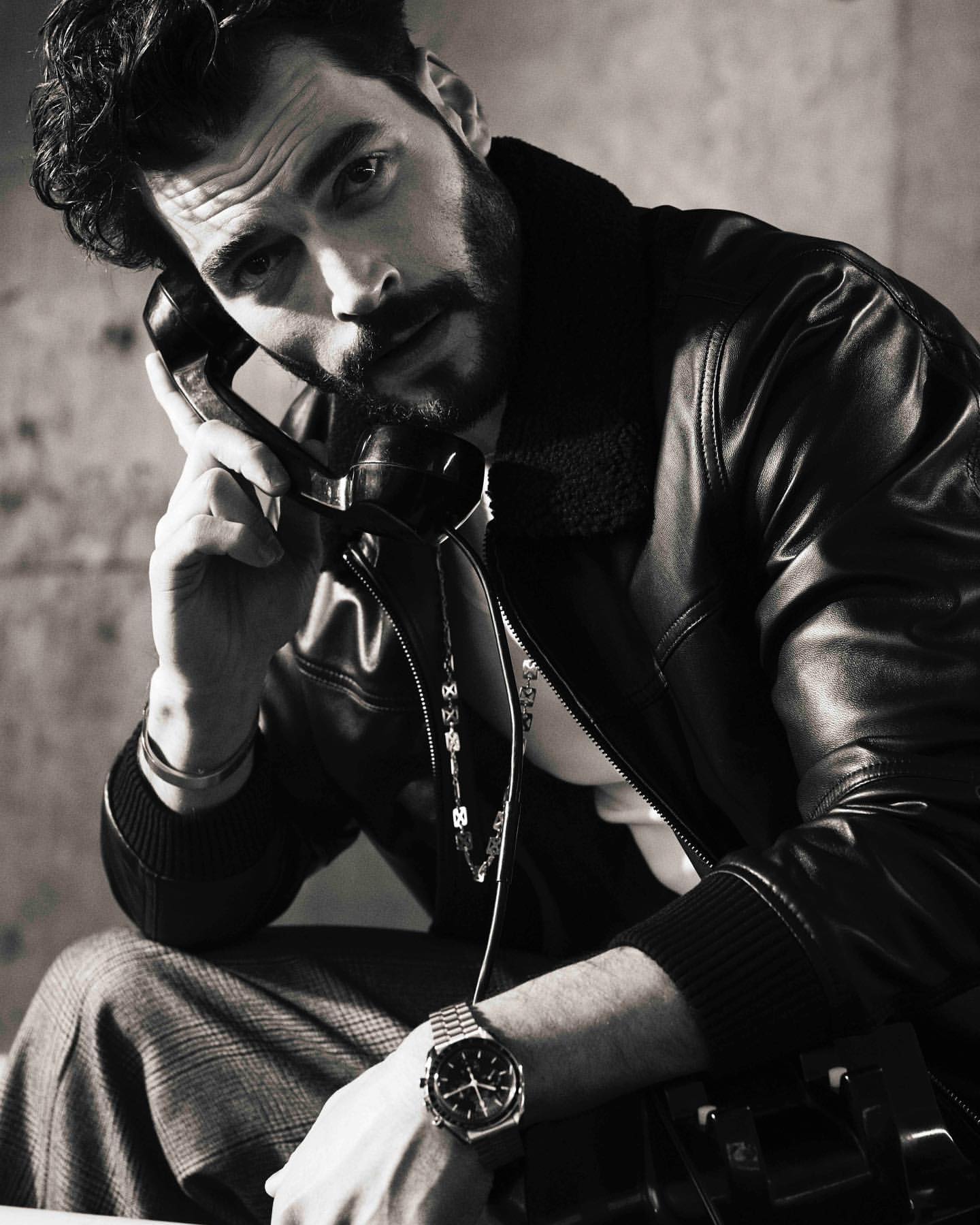 Monochrome portrait of a bearded man in a leather jacket holding an old telephone handset to his ear