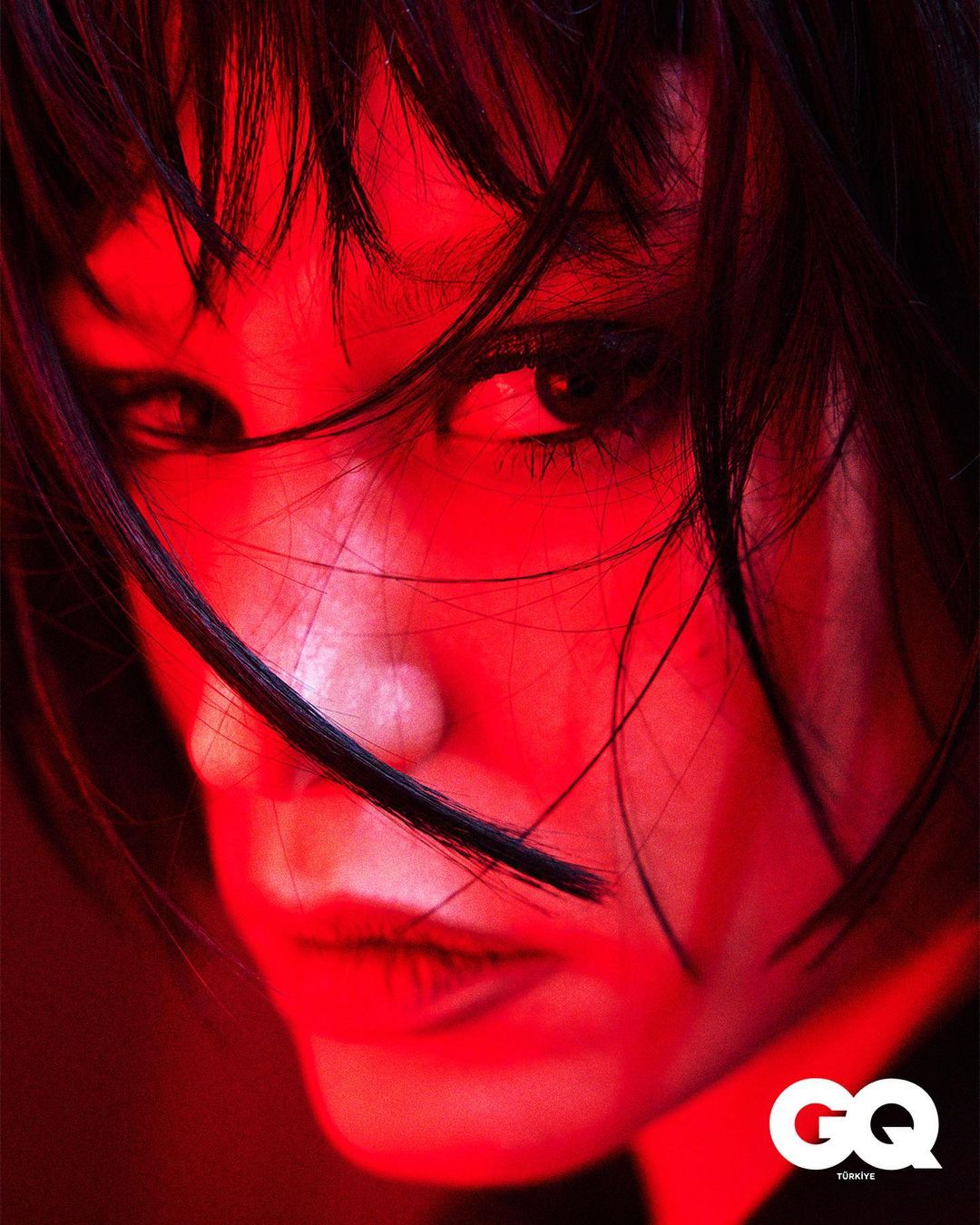 Close-up portrait of a woman with dark hair under vibrant red lighting, featuring the GQ logo in the corner and emphasizing her intense gaze.