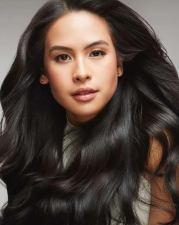 Close-up portrait of a woman with long dark wavy hair wearing a white top against a grey background by Erez Sabag.