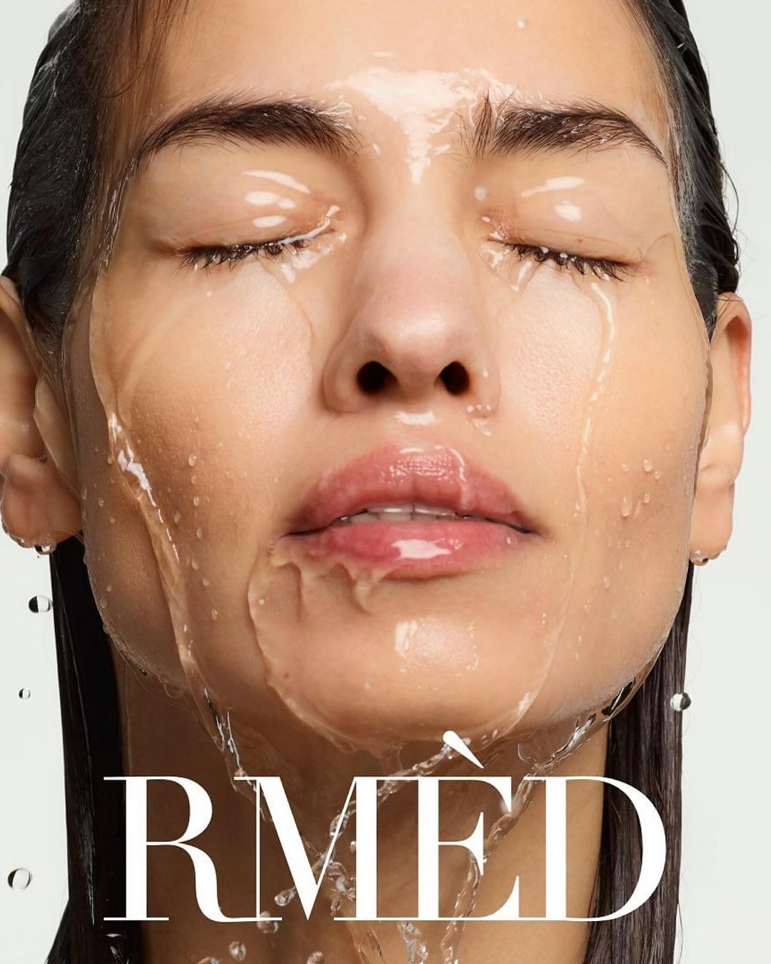 Close-up of a woman's face with water running down it, showcasing a beauty or skincare product in a studio setting.