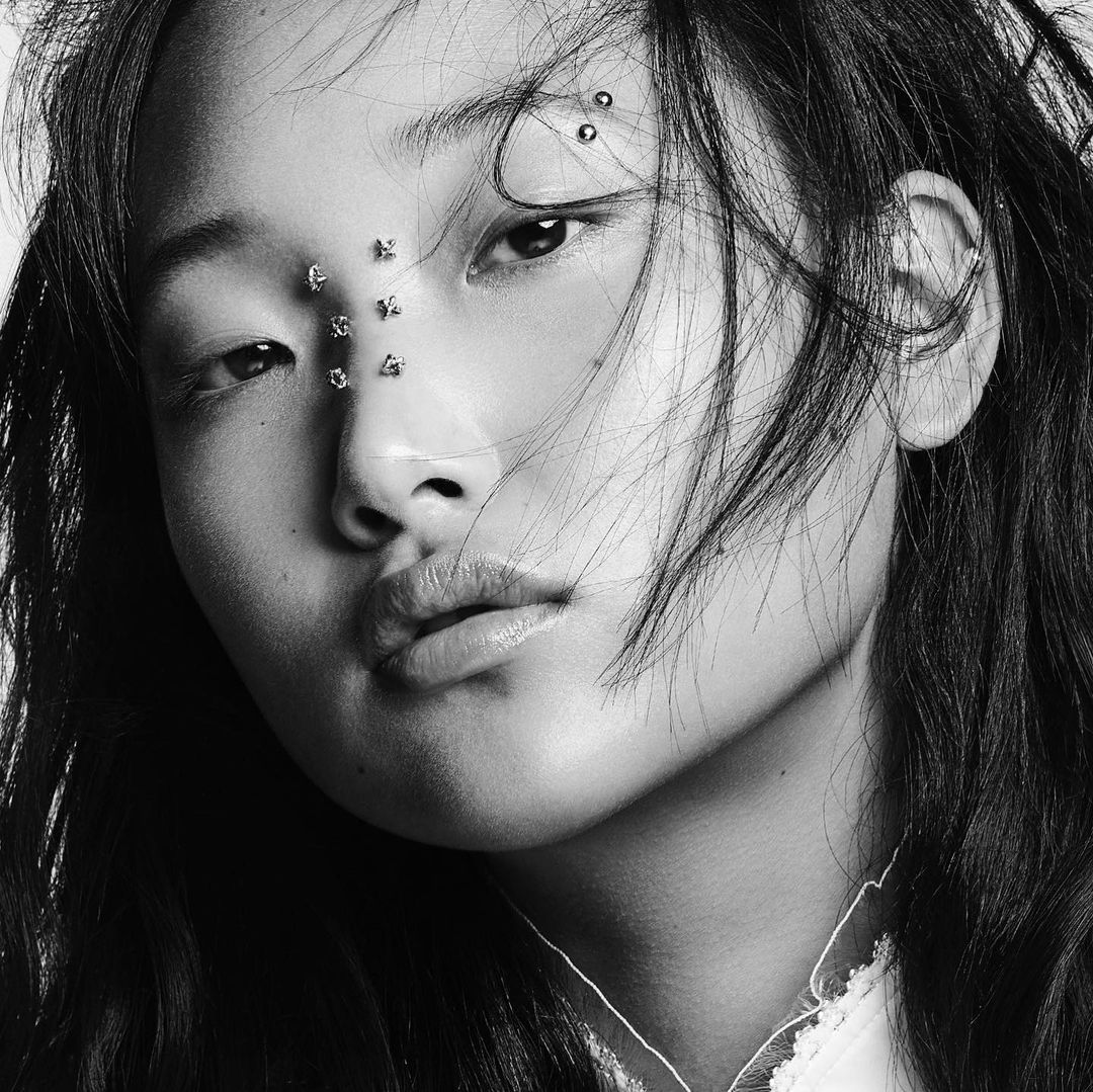 Close-up black and white portrait of an Asian woman with face jewelry, showcasing beauty and personal style in a minimalist setting.