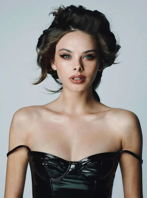 Portrait of a beautiful woman with dark hair styled in curlers, wearing a black shiny strapless top against a neutral background.