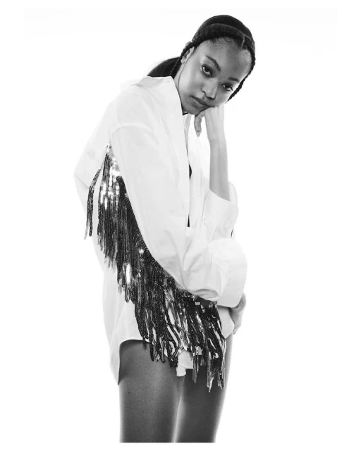 Black and white fashion portrait of an adult woman wearing a white dress shirt with beaded fringe, posing in a photo studio.