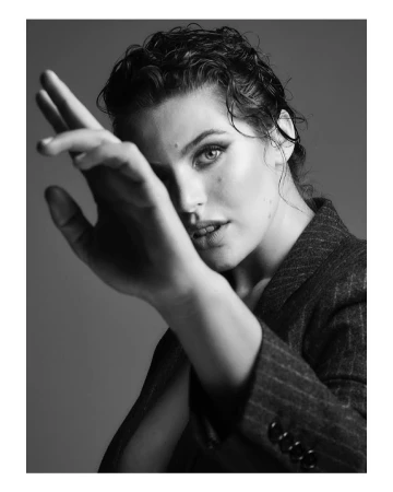 Portrait of a woman with wet hair wearing a pinstripe blazer holding her hand up towards the camera in monochrome.