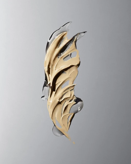 Tan foundation swatch with a clear gel-like medium on a gradient grey backdrop. Beauty product photography.