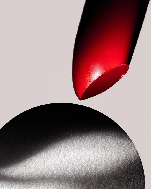 Close-up product shot of red lipstick above a textured black circle against a light grey background, studio lighting, beauty product photography.