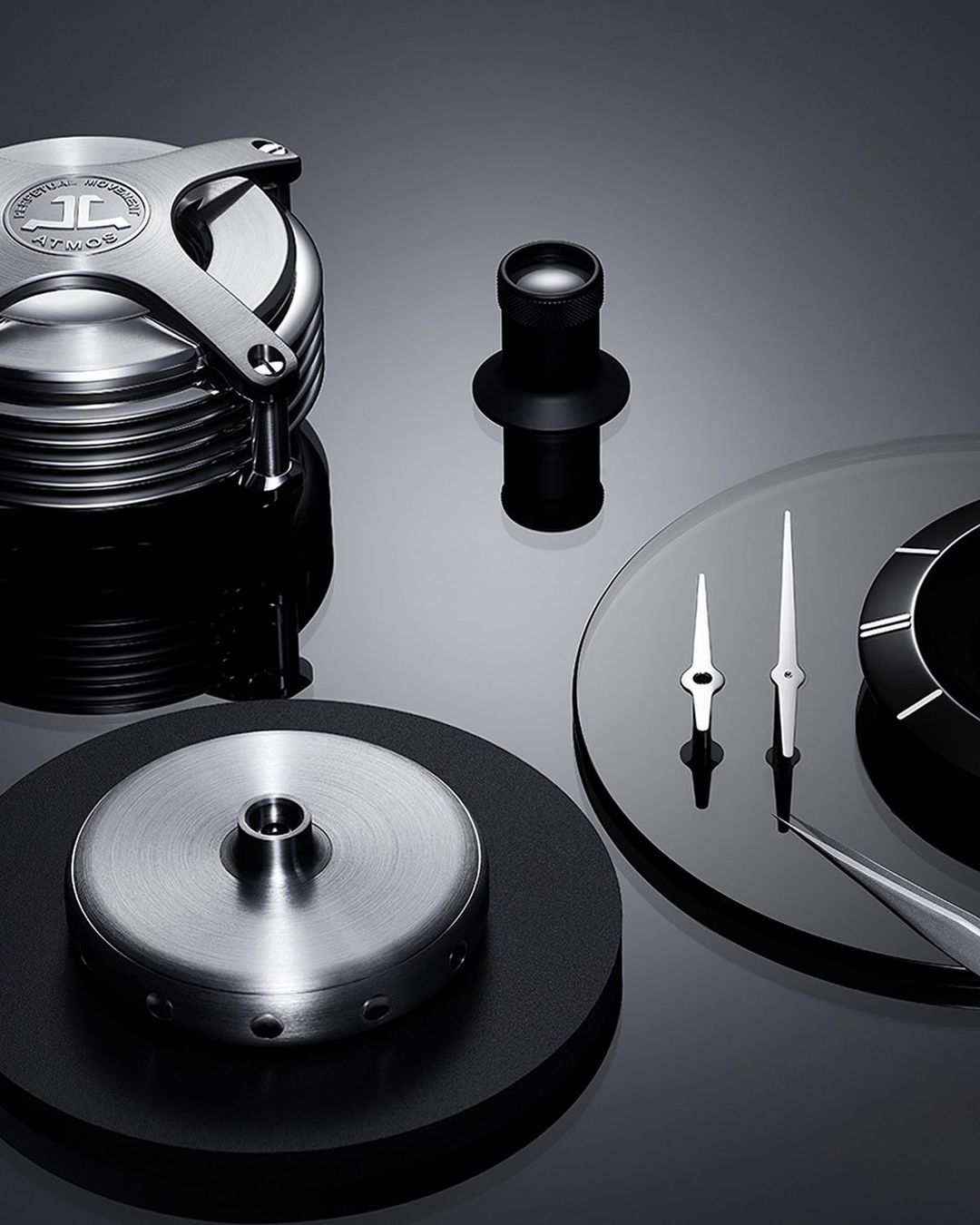 Close-up product shot featuring watch components on a glossy black surface. The scene is staged in a studio setting with controlled lighting.