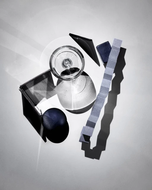Overhead shot of arranged transparent glass, opaque blue sphere, and geometric paper strips on a white background with shadows.