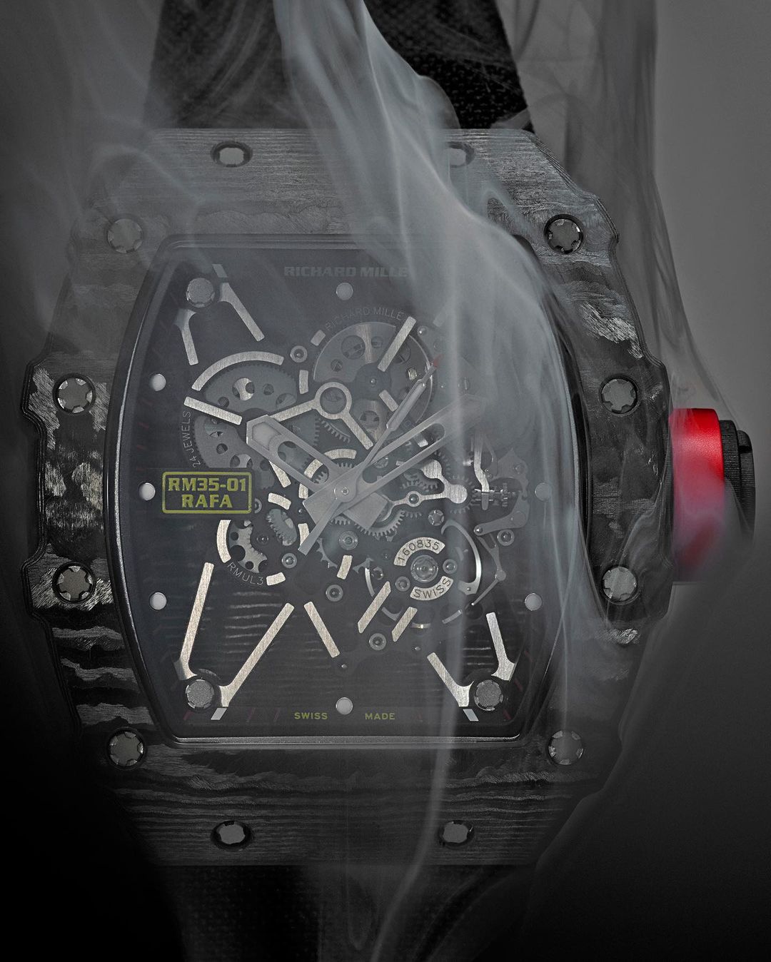 A close-up studio shot of a sophisticated black and silver wristwatch with an open-face dial, enveloped in wisps of white smoke against a gray backdrop.