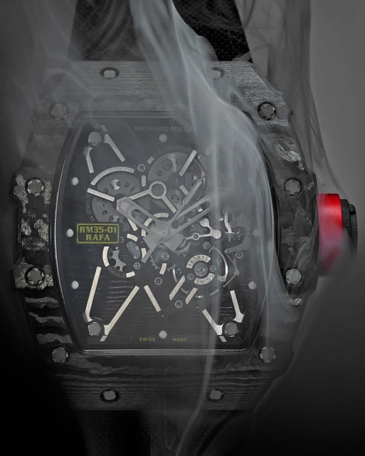 A close-up studio shot of a sophisticated black and silver wristwatch with an open-face dial, enveloped in wisps of white smoke against a gray backdrop.
