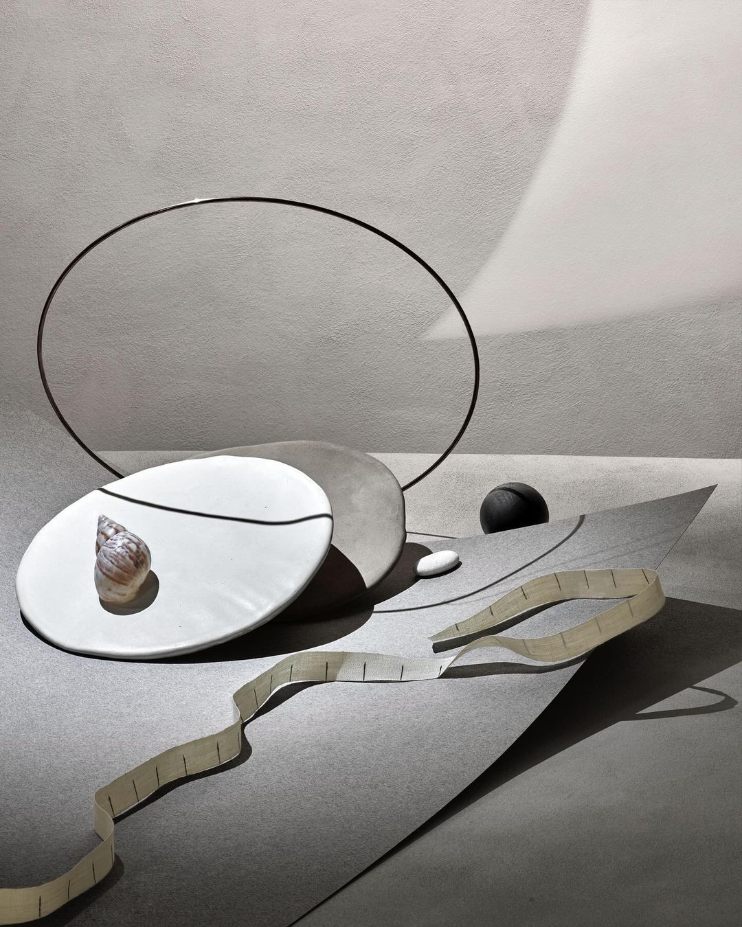 Still life photography featuring a seashell on a plate with geometric shapes and soft lighting in shades of gray and white.