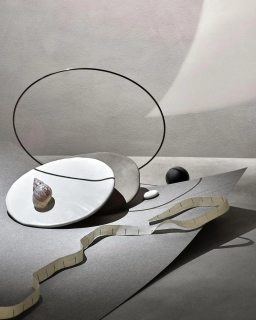 Still life photography featuring a seashell on a plate with geometric shapes and soft lighting in shades of gray and white.