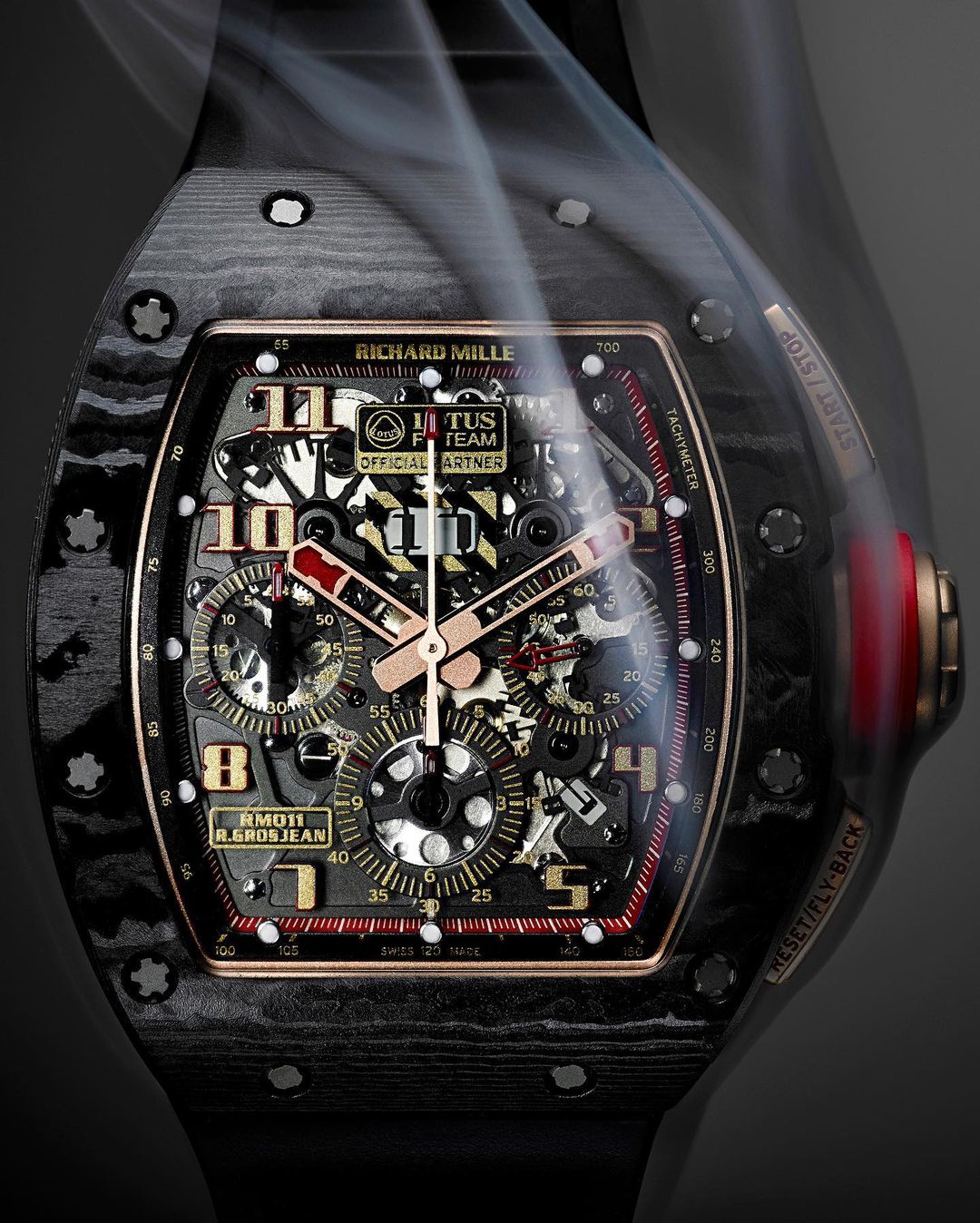 Luxury carbon fiber Richard Mille RM011 R. Grosjean wristwatch close-up, featuring an intricate skeleton dial, red accents, and smoke overlay.