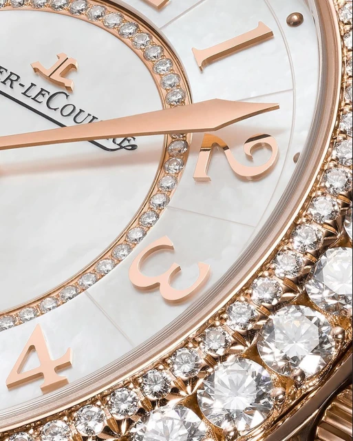 Close-up of a luxurious watch with rose gold hands and diamond embellishments against a white mother-of-pearl face.