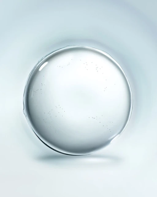 A clear, round droplet or gel sits against a soft, light blue gradient background, highlighted by a central reflection point.