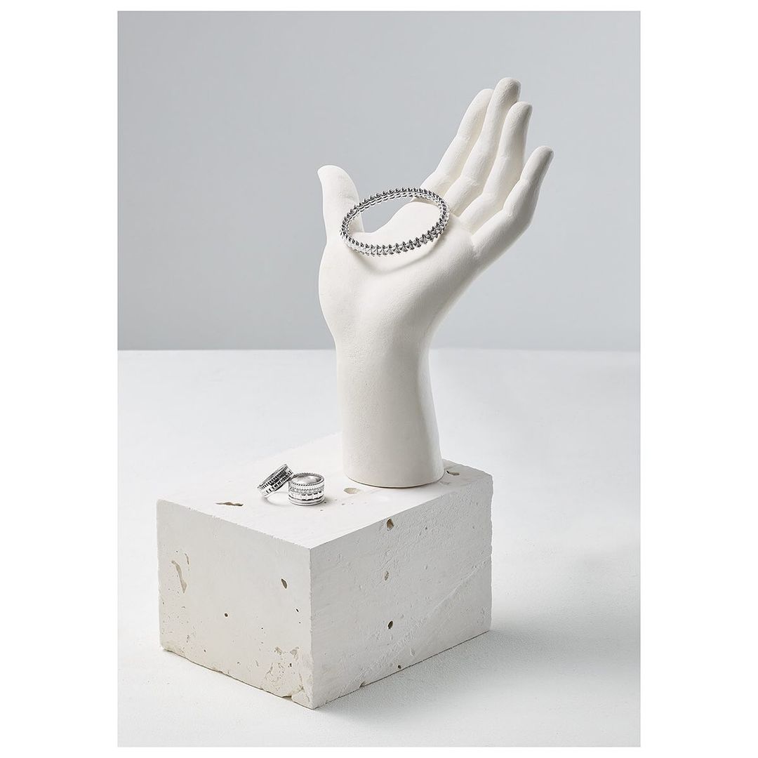 Jewelry display featuring a white hand mannequin holding a silver beaded bracelet, and silver rings displayed on a concrete block.