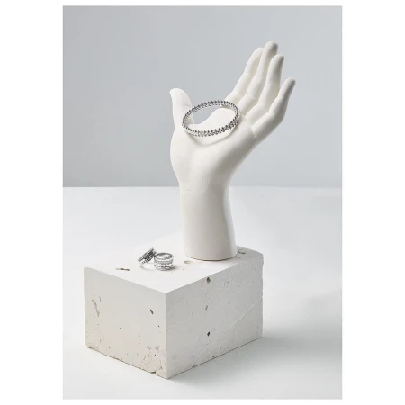 Jewelry display featuring a white hand mannequin holding a silver beaded bracelet, and silver rings displayed on a concrete block.