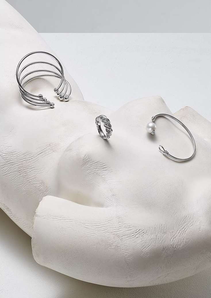 Silver cuff bracelets, silver ring, and silver open bangle with pearl set on a white plaster sculpture head, studio lighting.