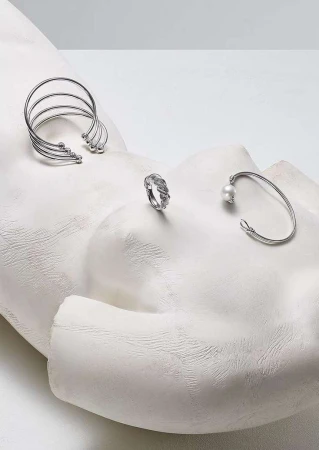 Silver cuff bracelets, silver ring, and silver open bangle with pearl set on a white plaster sculpture head, studio lighting.
