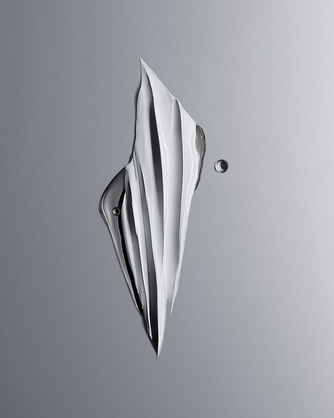 Abstract image of white skincare cream swatch with small water droplets on a gradient grey background in studio lighting.