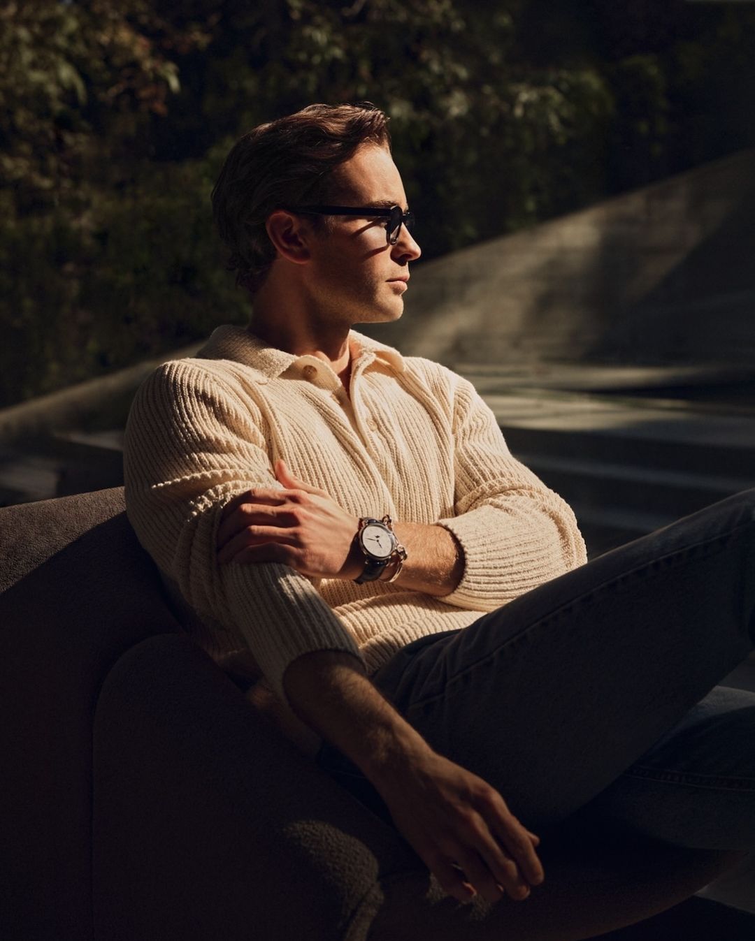 Man wearing a cream knit polo shirt and dark sunglasses seated in a chair, captured in warm sunlight by Eric Michael Roy.