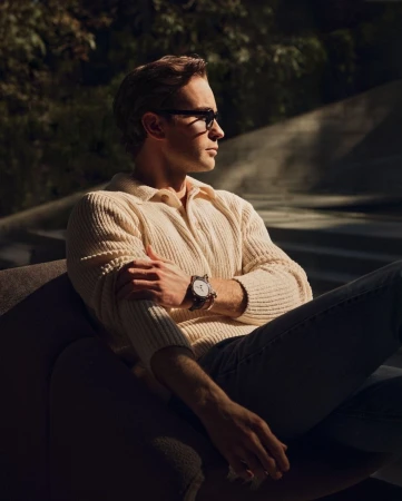 Man wearing a cream knit polo shirt and dark sunglasses seated in a chair, captured in warm sunlight by Eric Michael Roy.