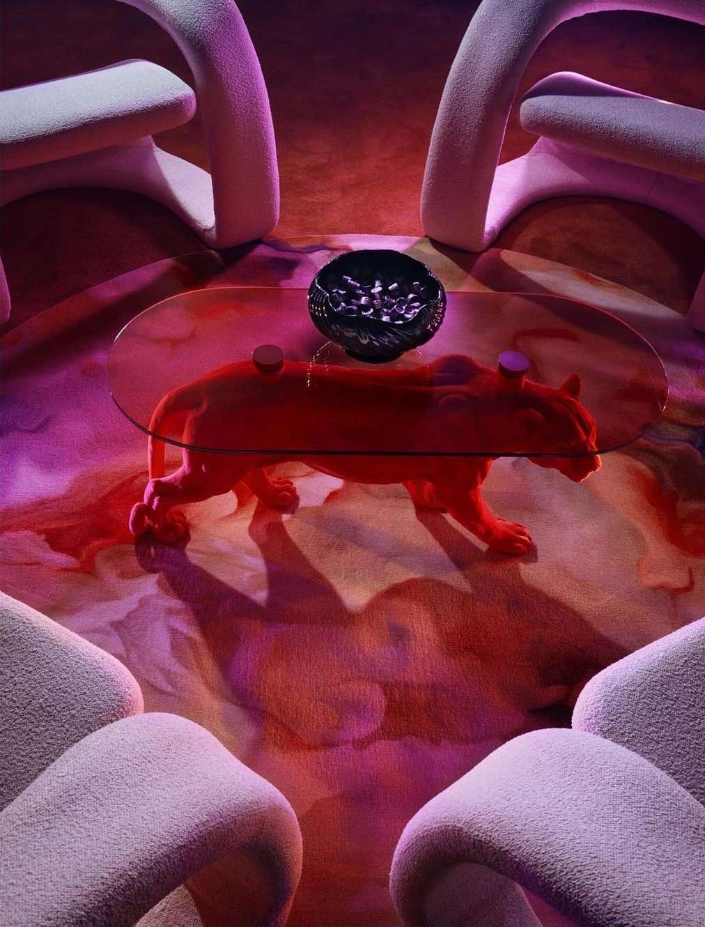 Interior design of living room with modern, sculptural chairs, red jaguar coffee table under glass, and patterned purple and red rug.