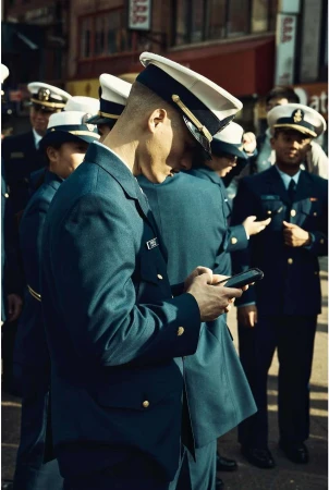 Man in military service dress uniform and peaked cap looking down at smartphone outdoors